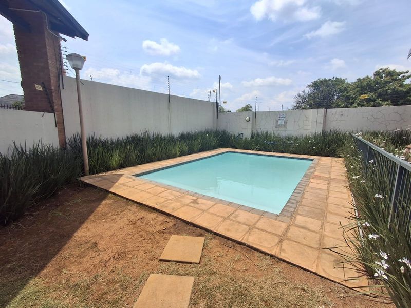 A private swimming pool area featuring a tiled surround, perimeter wall with electric fencing, and established garden borders.