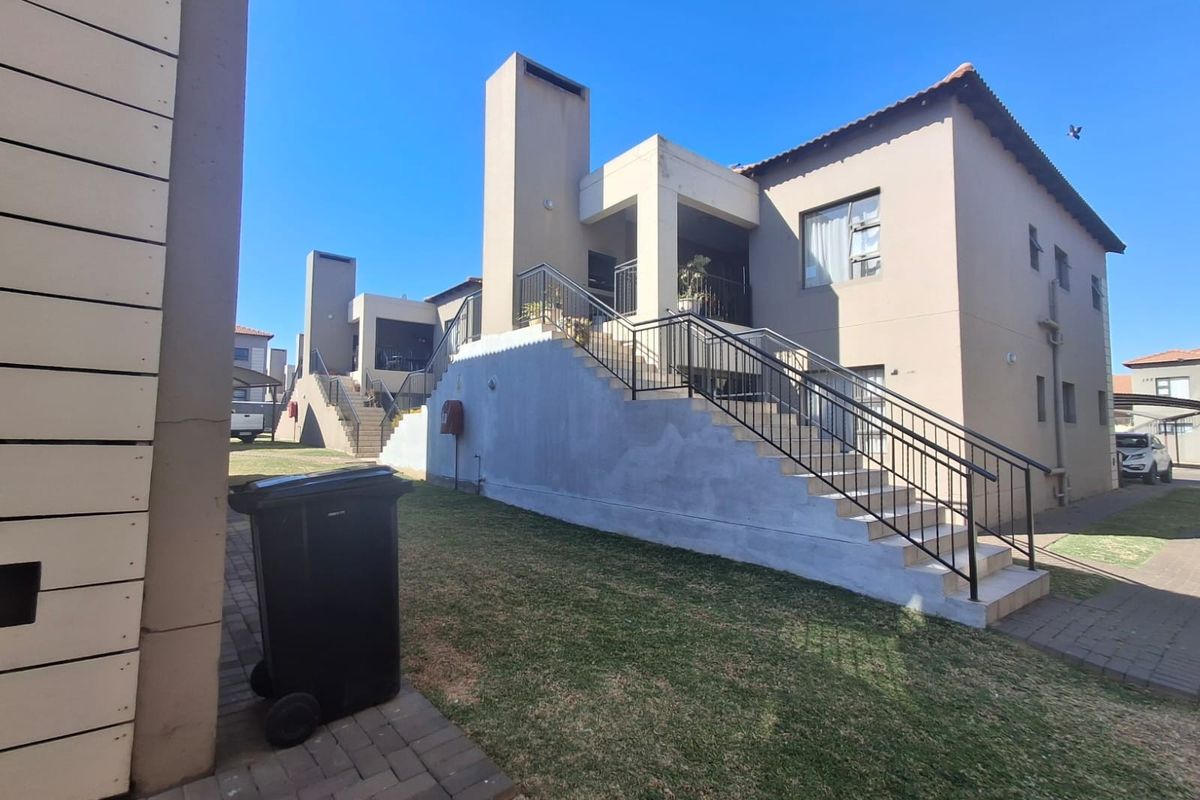 Rear view of the apartment complex featuring an external staircase with metal railings, paved walkways, and a shared lawn area.