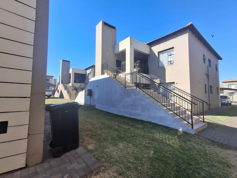 Rear view of the apartment complex featuring an external staircase with metal railings, paved walkways, and a shared lawn area.