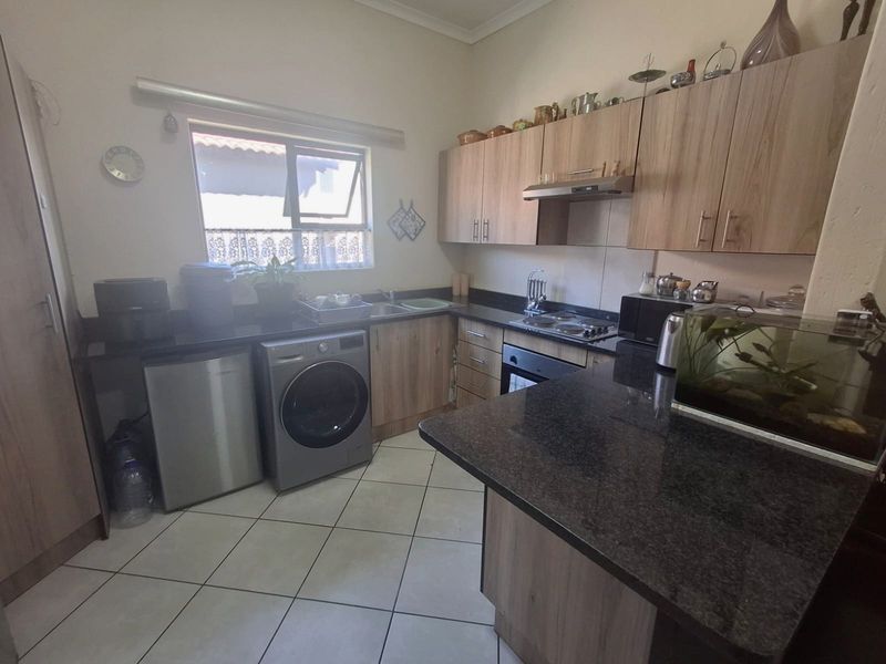 Functional kitchen featuring wood-look cabinetry, dark granite countertops, built-in oven, hob, extractor fan, and tiled flooring with space for under-counter appliances.