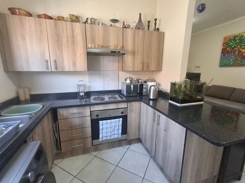 A functional kitchen featuring wood-look laminate cabinetry, dark granite countertops, a built-in oven with electric hob, and tiled flooring.