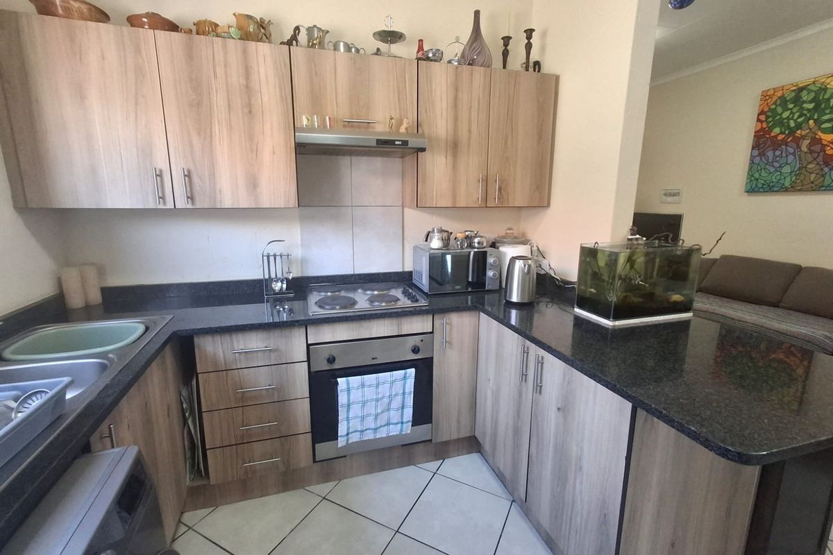 A functional kitchen featuring wood-look laminate cabinetry, dark granite countertops, a built-in oven with electric hob, and tiled flooring.