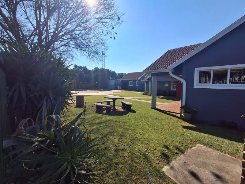 A view of the rear exterior of the apartment complex, featuring a well-maintained lawn, paved pathways, and a covered patio area.