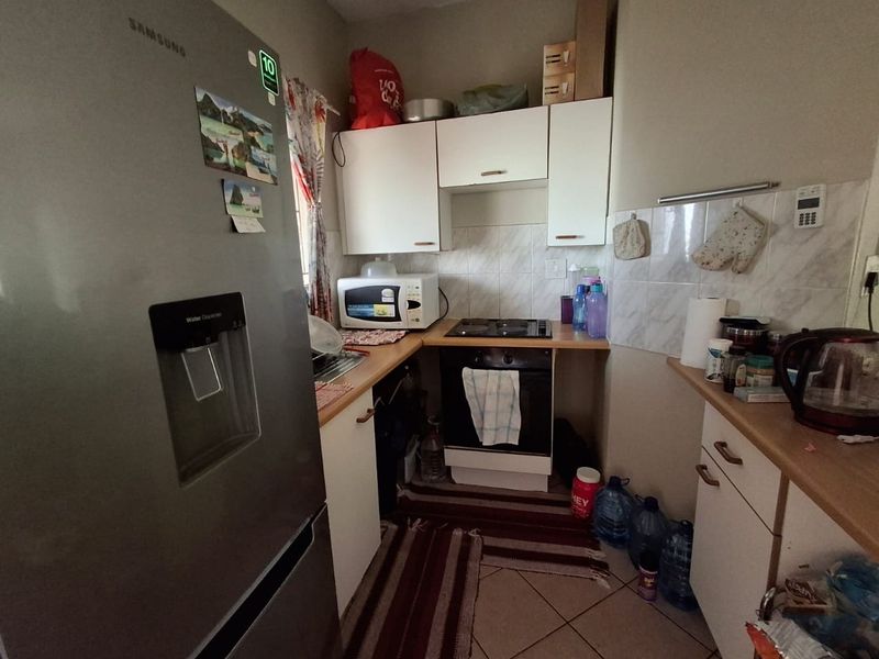 Compact kitchen featuring white cabinetry, laminate countertops, tiled backsplash, and built-in oven with electric hob.