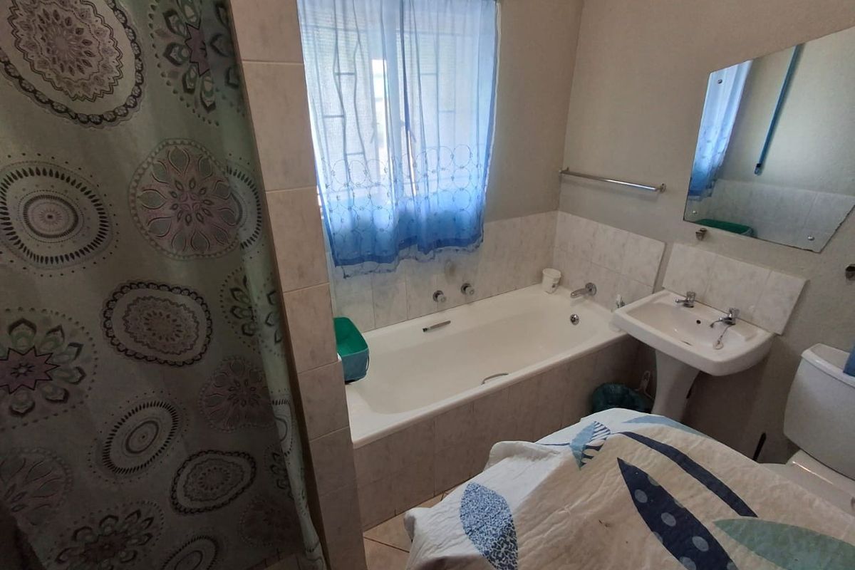 A functional bathroom featuring a built-in bathtub, pedestal washbasin, toilet, and wall-mounted mirror with tiled splashbacks.