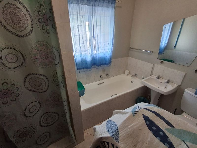 A functional bathroom featuring a built-in bathtub, pedestal washbasin, toilet, and wall-mounted mirror with tiled splashbacks.