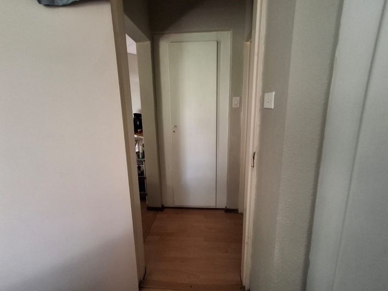 A functional hallway featuring laminate flooring and a built-in storage cupboard, providing access to adjacent rooms within the apartment.