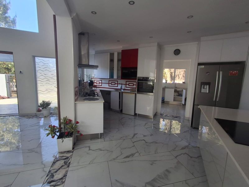 Modern open-plan kitchen featuring marble-look floor tiles, built-in appliances, and an adjoining scullery area with ample cabinetry.