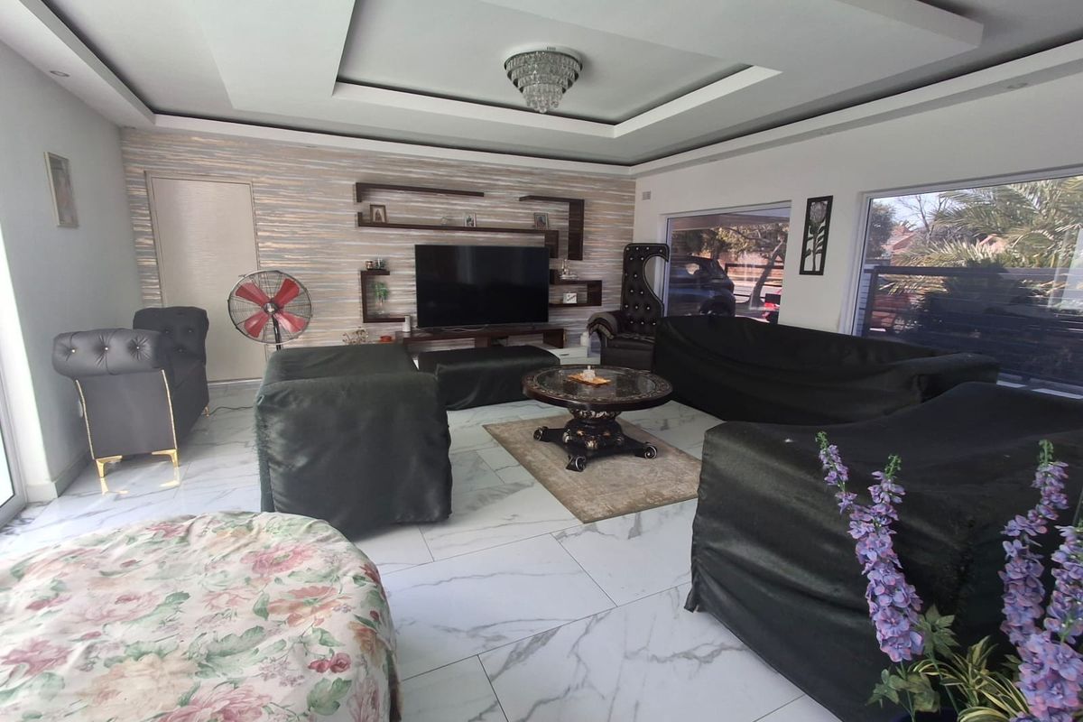 Spacious living room featuring marble-look floor tiles, a recessed ceiling with a crystal chandelier, and built-in wall shelving.