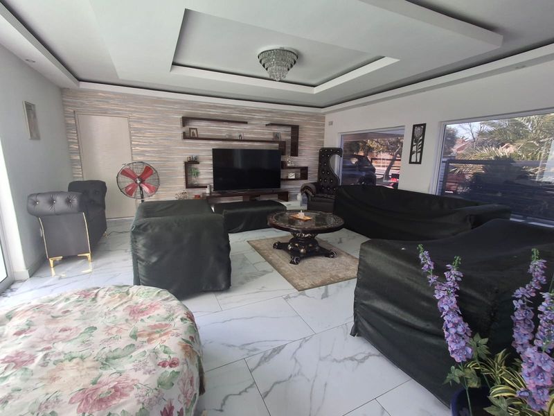 Spacious living room featuring marble-look floor tiles, a recessed ceiling with a crystal chandelier, and built-in wall shelving.