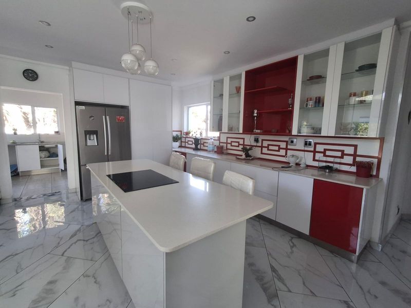 Modern kitchen featuring a central island with induction cooktop, quartz countertops, high-gloss cabinetry, and marble-look tiled flooring, with an adjacent scullery area.