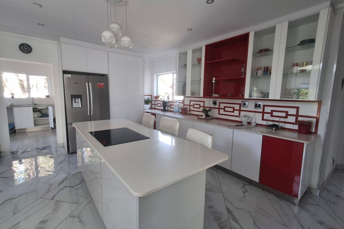 Modern kitchen featuring a central island with induction cooktop, quartz countertops, high-gloss cabinetry, and marble-look tiled flooring, with an adjacent scullery area.
