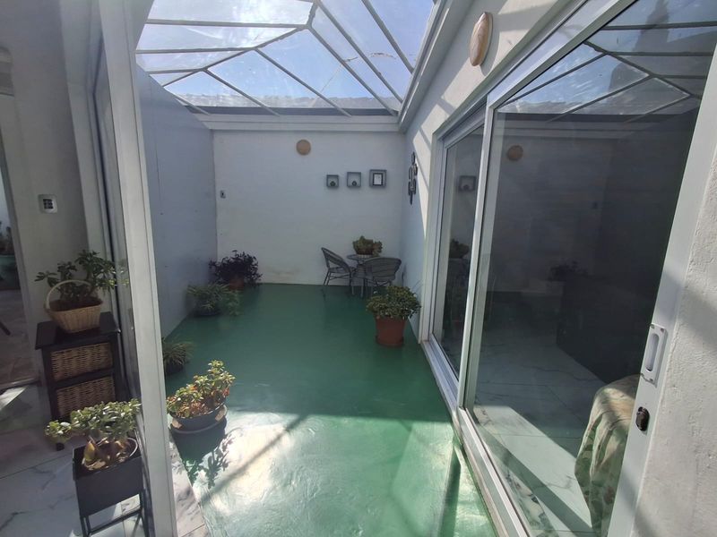 A covered patio area featuring a glass roof and sliding glass doors, providing a bright, semi-enclosed space for outdoor relaxation.