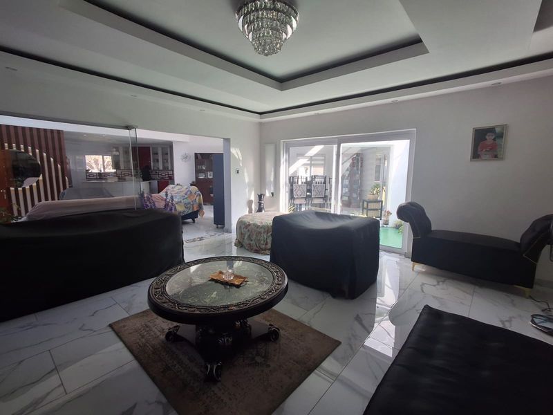 Spacious open-plan living area featuring high-gloss marble-look flooring, a decorative recessed ceiling with a crystal chandelier, and large sliding doors leading to the patio.