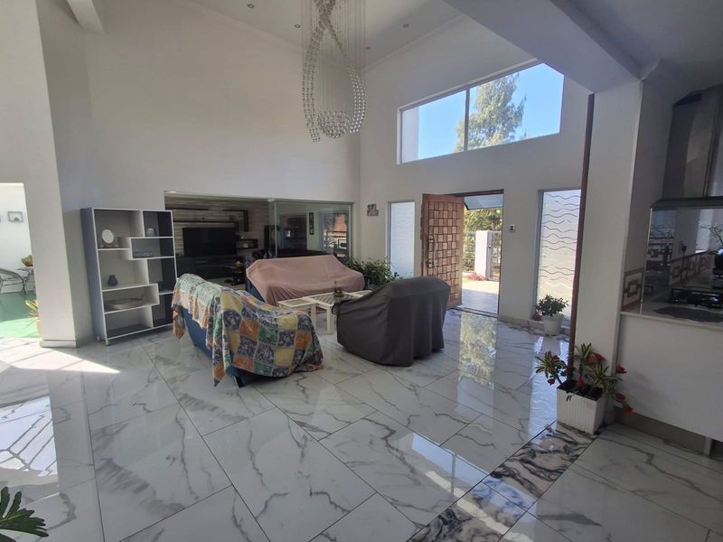 Spacious open-plan living area featuring high double-volume ceilings, large clerestory windows for natural light, and polished marble-look porcelain floor tiles throughout.