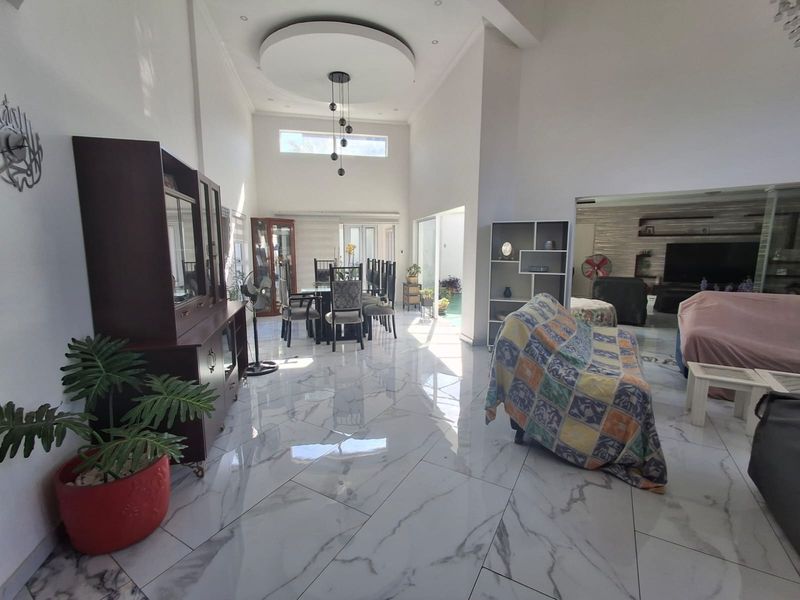 Spacious open-plan living and dining area featuring high ceilings, a decorative recessed ceiling detail, and polished marble-look floor tiles throughout.