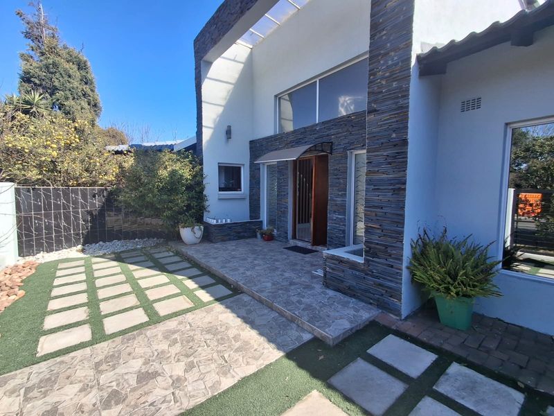 Front entrance featuring modern stone cladding, a tiled patio area, and a well-maintained garden with paver walkways and artificial lawn.