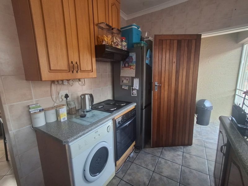 A compact kitchen featuring wooden cabinetry, tiled splashbacks, a built-in oven with hob, and tiled flooring, providing a functional workspace.