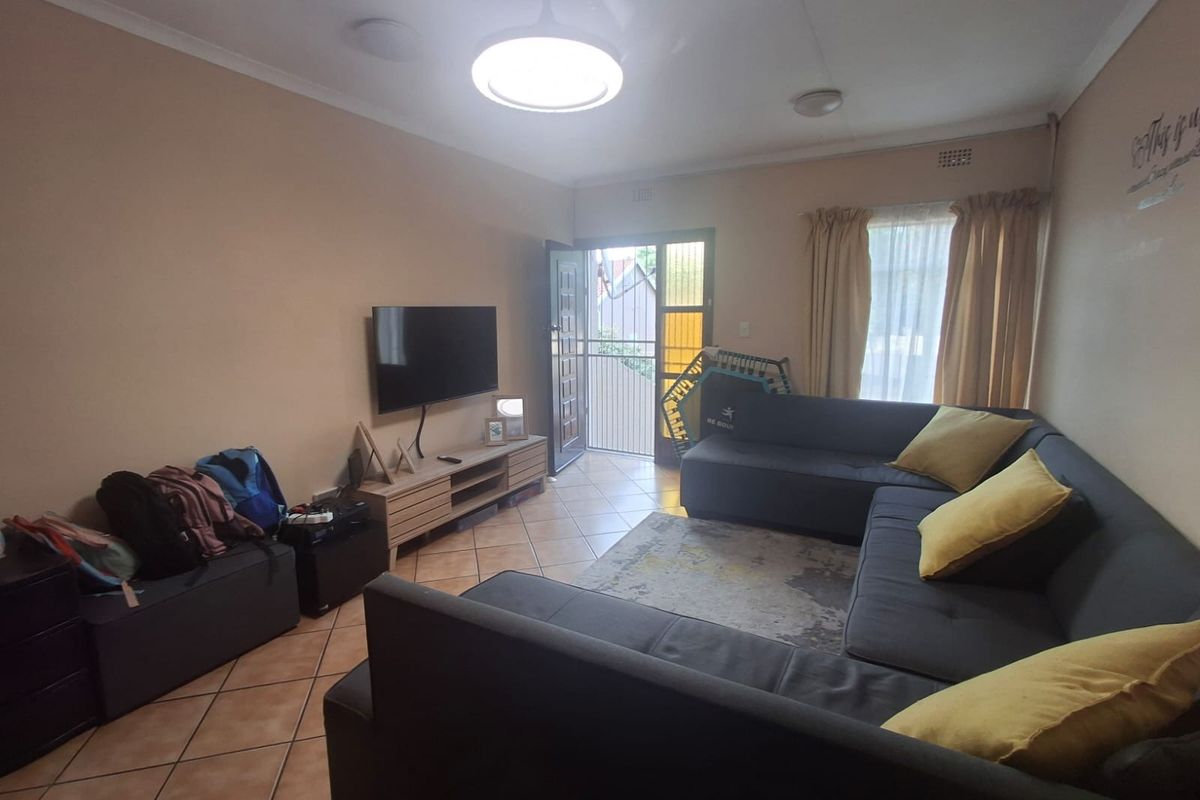 A comfortable living room featuring tiled flooring, a ceiling light fixture, and direct access to an exterior area through a security gate.