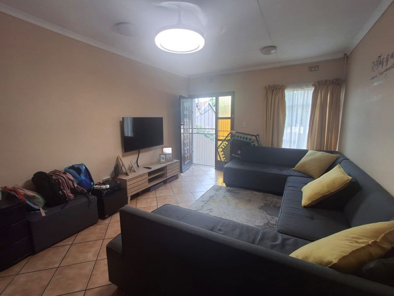 A comfortable living room featuring tiled flooring, a ceiling light fixture, and direct access to an exterior area through a security gate.