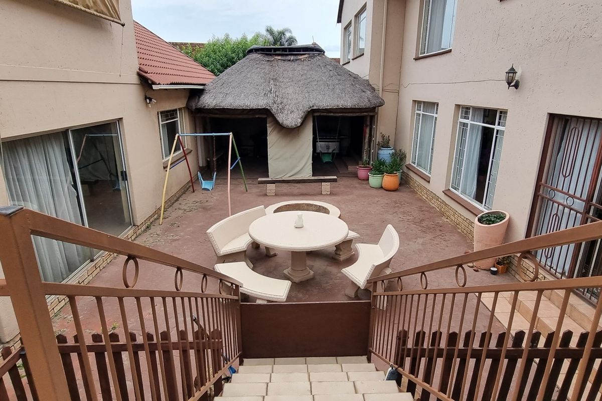 A paved rear courtyard area featuring a thatched lapa, accessible via a staircase, providing a functional outdoor entertainment space.
