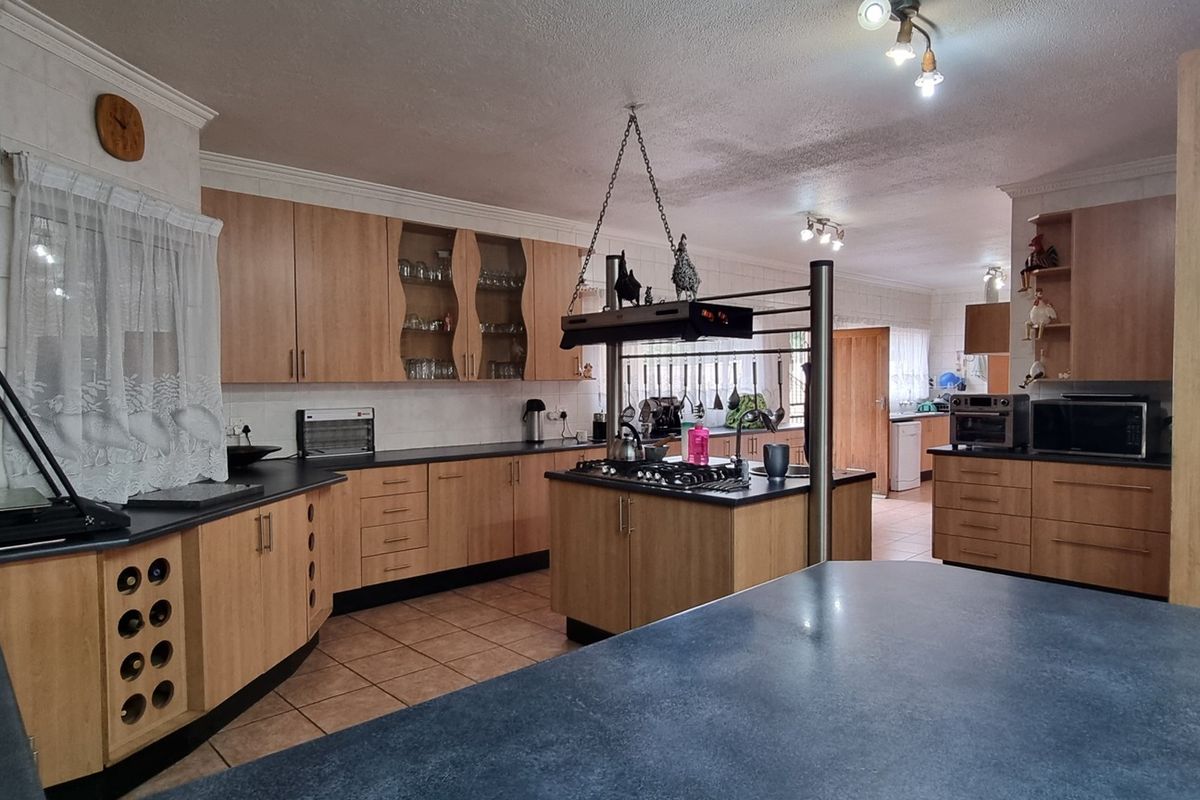 Spacious kitchen featuring light wood cabinetry, dark countertops, a central island with a built-in gas hob, and tiled flooring.