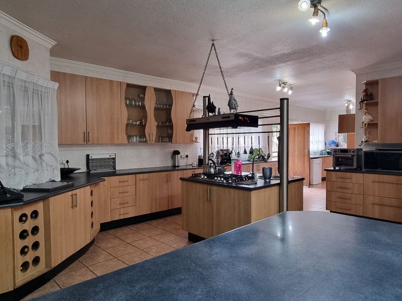 Spacious kitchen featuring light wood cabinetry, dark countertops, a central island with a built-in gas hob, and tiled flooring.