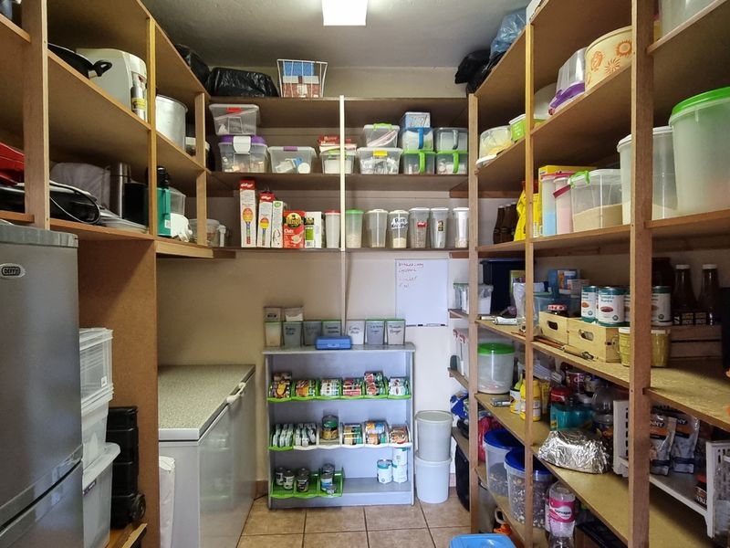 A functional walk-in pantry or scullery area featuring extensive built-in wooden shelving for organized storage and tiled flooring.