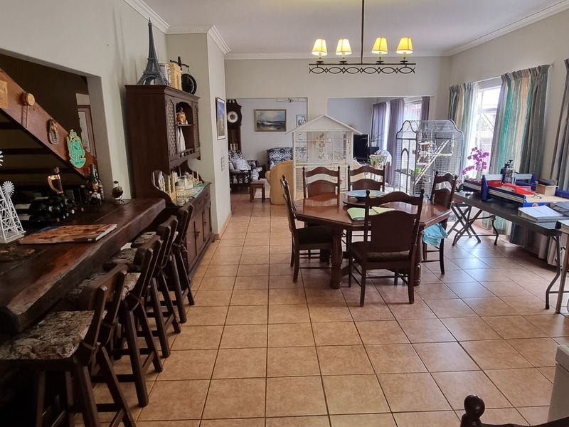 Spacious open-plan living and dining area featuring ceramic floor tiles, a built-in wooden bar, and a staircase leading to the upper level.
