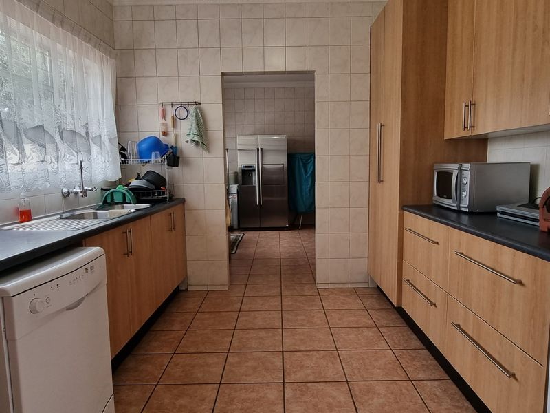 Functional kitchen featuring wood-look cabinetry, tiled splashbacks, dark laminate countertops, and a convenient adjoining scullery area with additional storage.