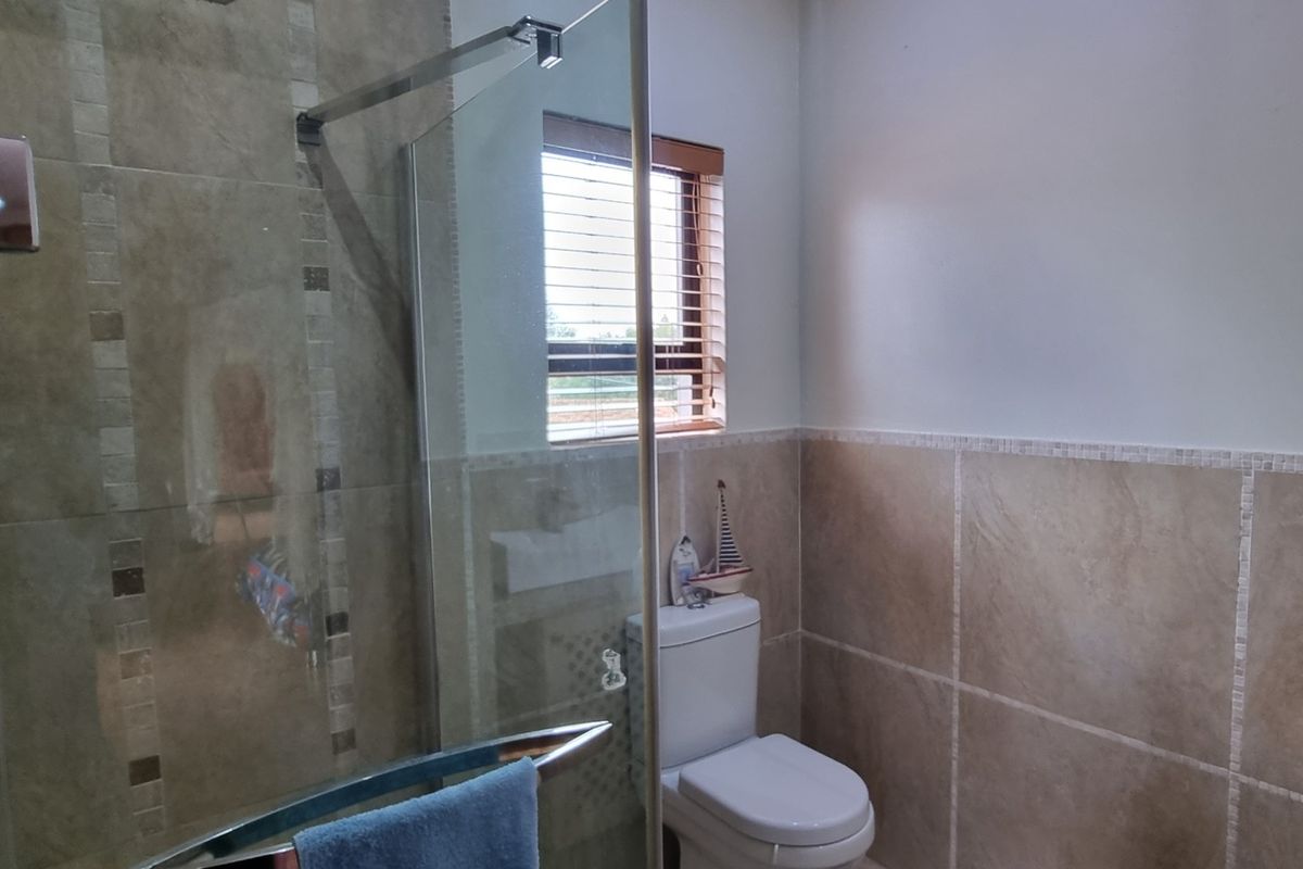A modern bathroom featuring a glass-enclosed shower with tiled walls, a white toilet, and a window with fitted wooden blinds.