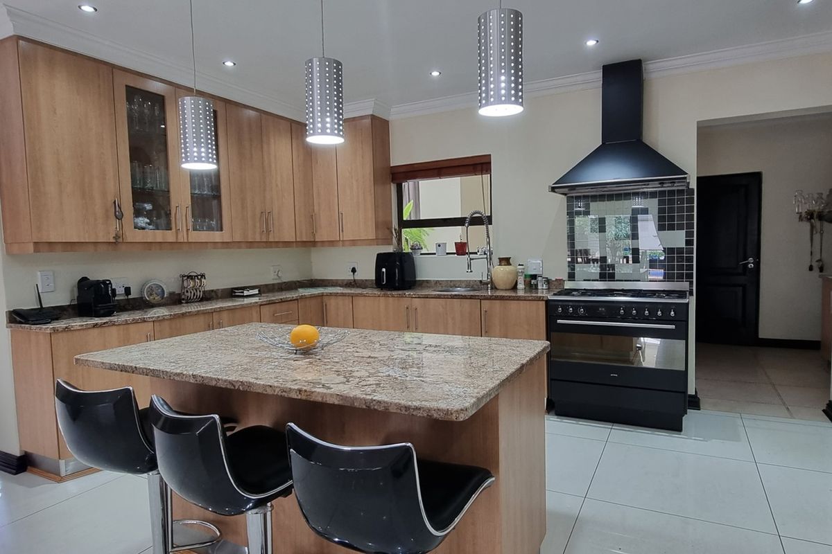 A well-maintained kitchen featuring light wood cabinetry, granite countertops, a central island, and a black freestanding oven with a matching extractor fan.