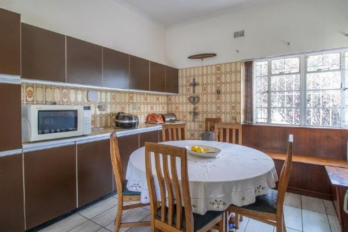 A dated kitchen featuring brown cabinetry, patterned wall tiles, tiled flooring, and a built-in window bench seat.