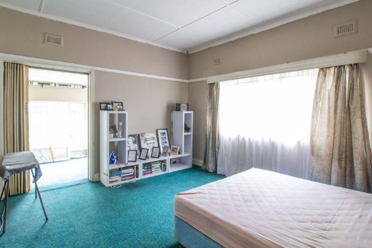 A spacious bedroom featuring green carpeting, large windows, and direct access to an adjoining patio area through a folding door.