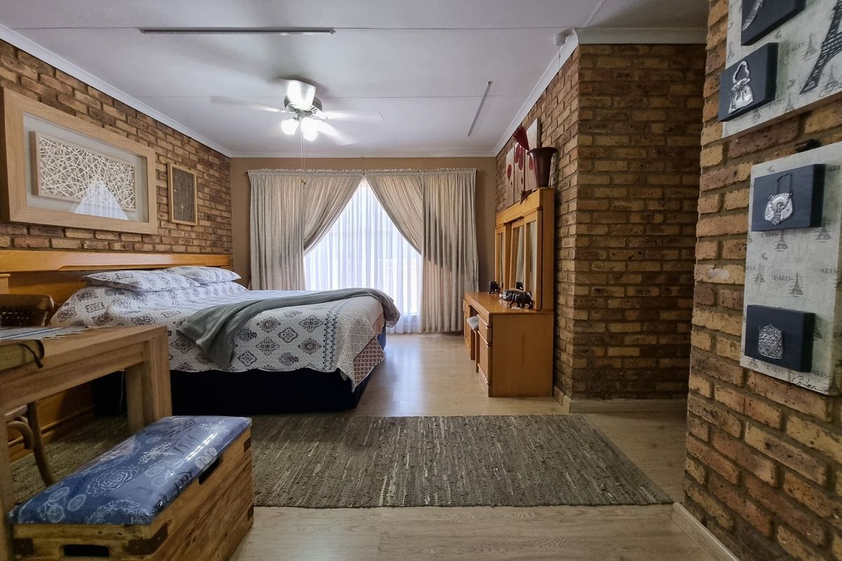 Spacious bedroom featuring exposed brick feature walls, light wood-look flooring, and a ceiling fan, offering a warm and rustic aesthetic.