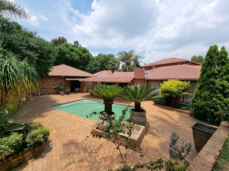 Spacious outdoor pool area featuring extensive brick paving, established garden beds, and a well-maintained swimming pool set against the rear facade of the house.