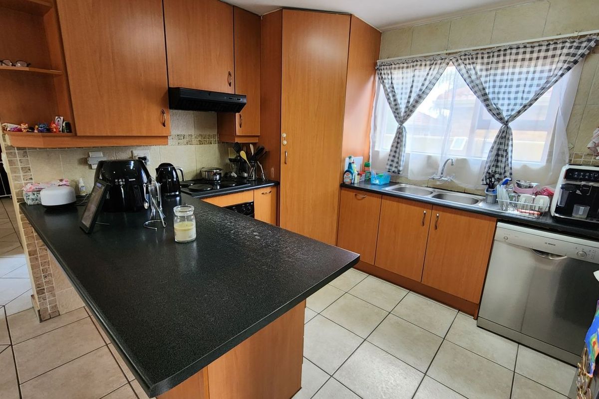 A functional kitchen featuring laminate cabinetry, dark countertops, a double basin sink, and built-in cooking appliances with tiled flooring and backsplash.