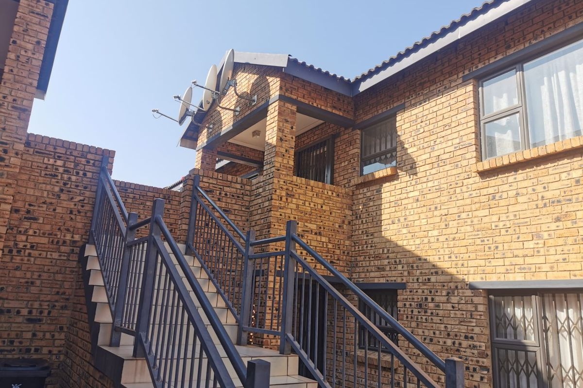 Exterior view of a face brick townhouse featuring an external staircase with metal balustrades and security gates leading to the upper level.