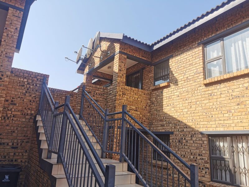 Exterior view of a face brick townhouse featuring an external staircase with metal balustrades and security gates leading to the upper level.