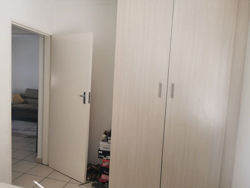 A bedroom featuring light wood-finish built-in wardrobes and tiled flooring, with a view into an adjacent living area.