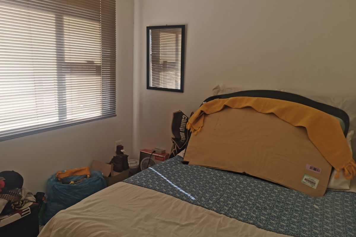 A bedroom featuring a window with venetian blinds and neutral wall finishes, providing a functional space for rest.