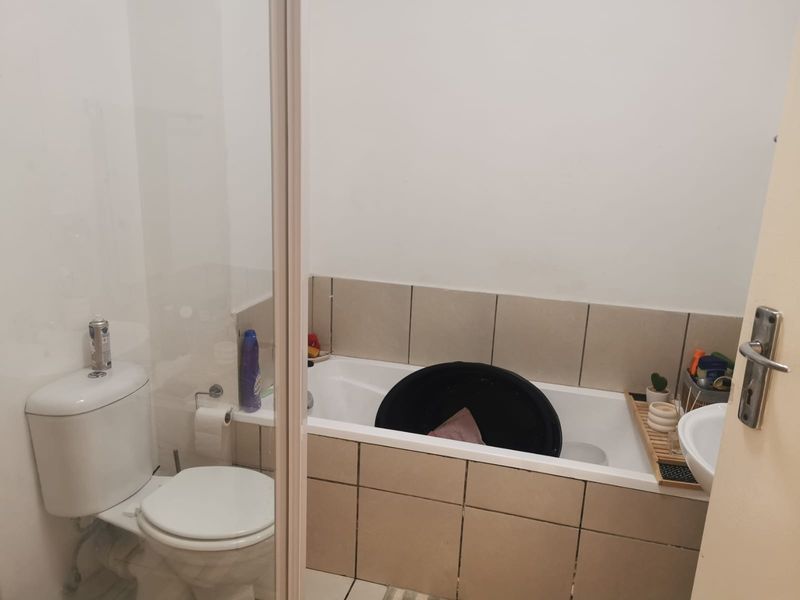 A functional bathroom featuring a bathtub with tiled surround, a standard toilet, and a basin, requiring some maintenance to the tile grout.