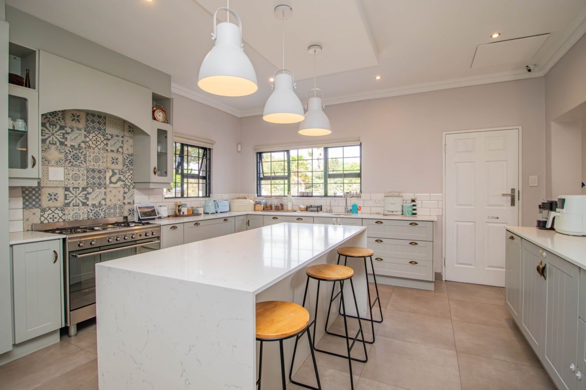 Modern kitchen featuring a large central island with quartz countertops, shaker-style cabinetry, a gas range with decorative tiled backsplash, and ample recessed lighting.