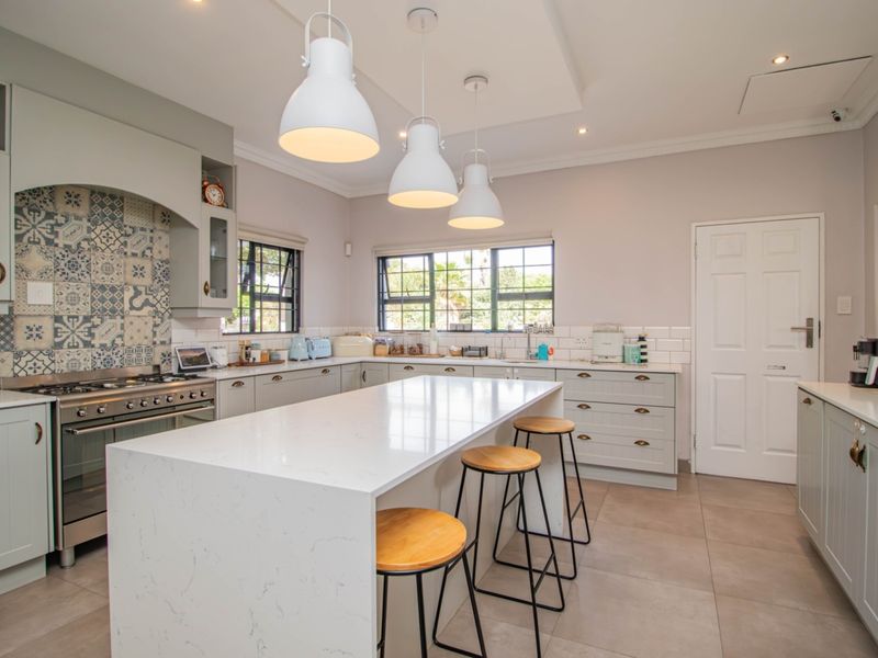 Modern kitchen featuring a large central island with quartz countertops, shaker-style cabinetry, a gas range with decorative tiled backsplash, and ample recessed lighting.