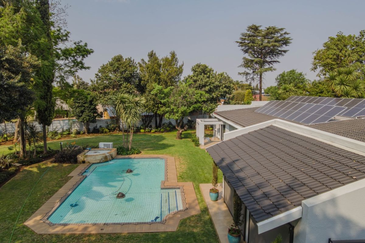 Aerial view of a residential property featuring a swimming pool with a safety net, a well-maintained garden, and solar panels installed on the roof.
