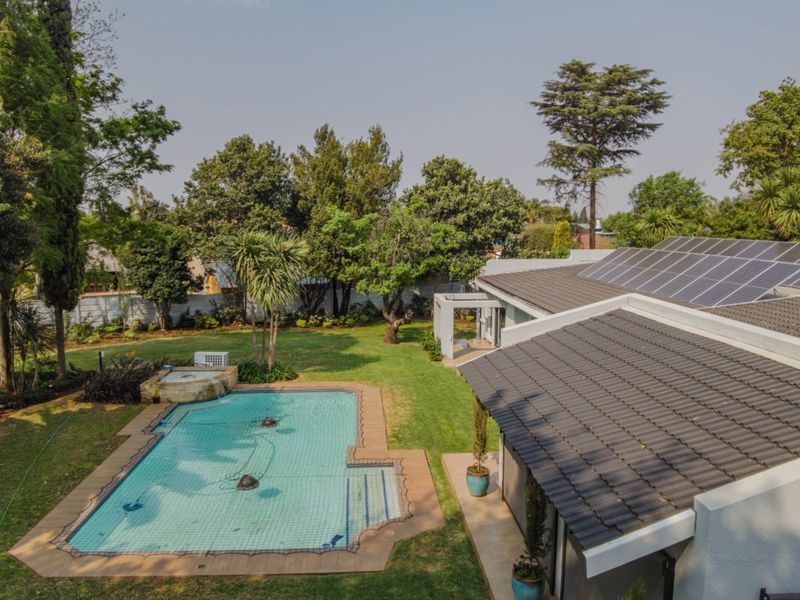 Aerial view of a residential property featuring a swimming pool with a safety net, a well-maintained garden, and solar panels installed on the roof.