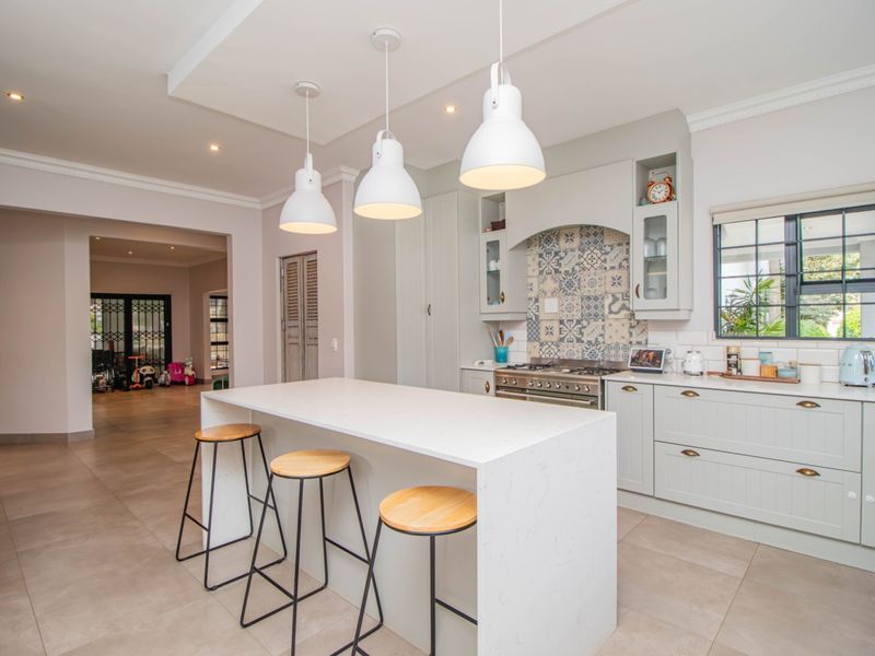 Modern kitchen featuring a central island with quartz countertops, gas stove, decorative tiled backsplash, and elegant pendant lighting in a bright, open-plan space.