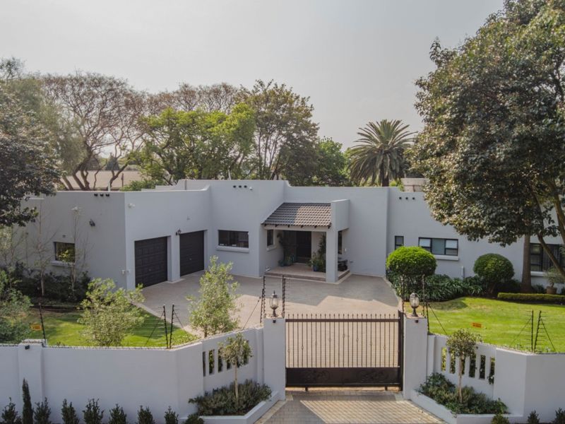 Aerial view of a well-maintained single-story residence featuring a paved driveway, double garage, secure gated entrance, and established garden.