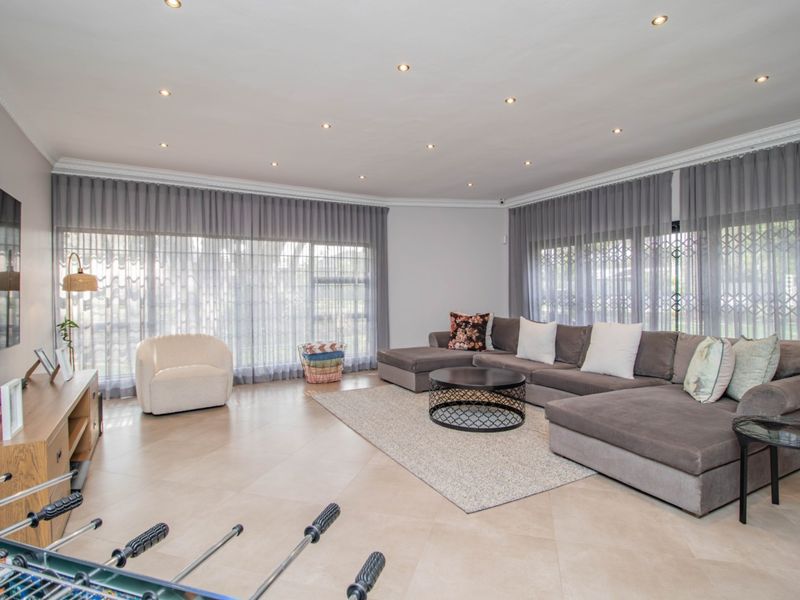 Spacious living room featuring large format floor tiles, recessed downlighting, crown molding, and expansive windows with integrated security gates.