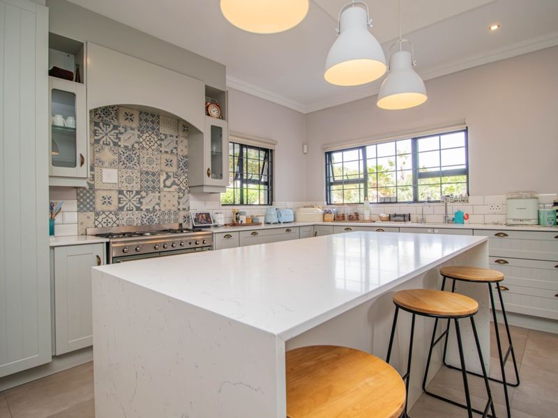 Modern kitchen featuring a large quartz island, patterned tile backsplash, gas range, and ample built-in cabinetry with a clean, contemporary aesthetic.